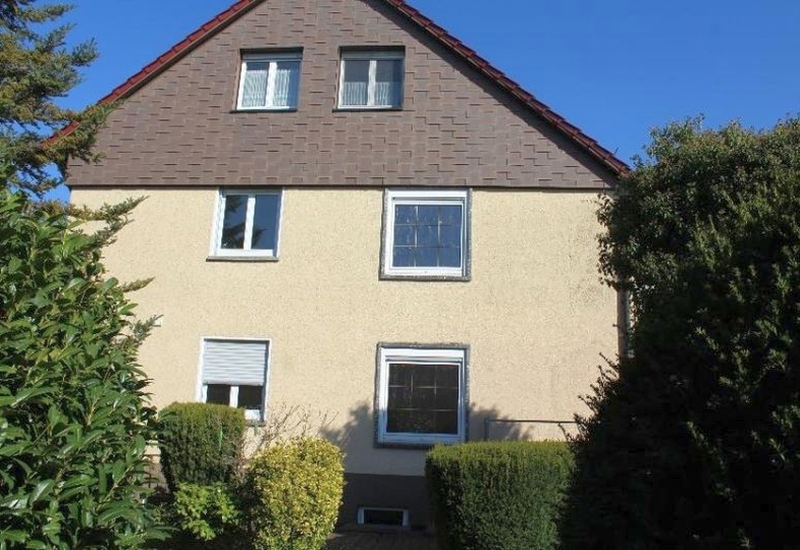Fassade eines Mehrfamilienhauses in Ostfildern-Kemnat, Heumadener Straße 53, mit braunem Satteldach, hellbeiger Putzfassade und mehreren Fenstern, umgeben von Hecken und Bäumen