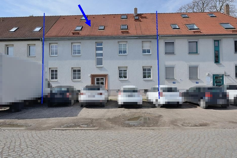 Mehrfamilienhaus mit rotem Ziegeldach und mehreren Dachfenstern, weiße Fassade, geparkte Fahrzeuge vor dem Gebäude