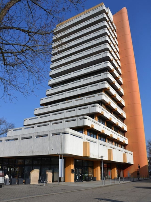 Mehrgeschossiges Wohn- und Geschäftshaus in Crailsheim, Postplatz 2, mit markanter orangefarbener Fassadenelement und grauen Balkonen unter blauem Himmel