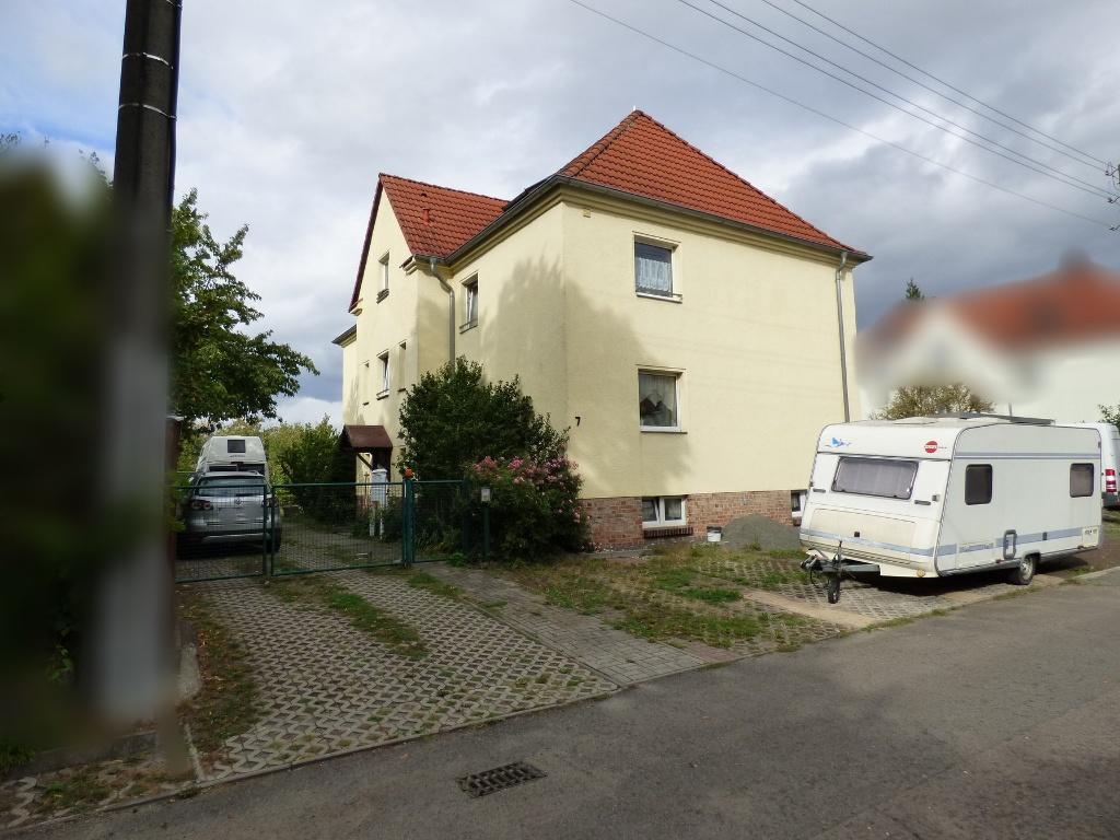 Seitenansicht eines zweistöckigen Wohnhauses mit rotem Ziegeldach und cremefarbener Fassade in Neukieritzsch, Neue Str. 7, mit geparktem Wohnwagen vor dem Grundstück