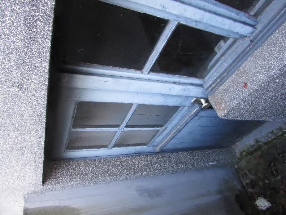 Eingangstür mit Glasteilen und Türknauf, eingebettet in eine strukturierte Fassade, Ansicht von oben links
