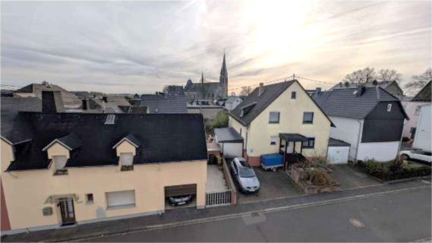 Seitenansicht eines Wohnhauses mit dunklem Dach, gelber Fassade, Garage und angrenzenden Häusern in einer Wohnstraße