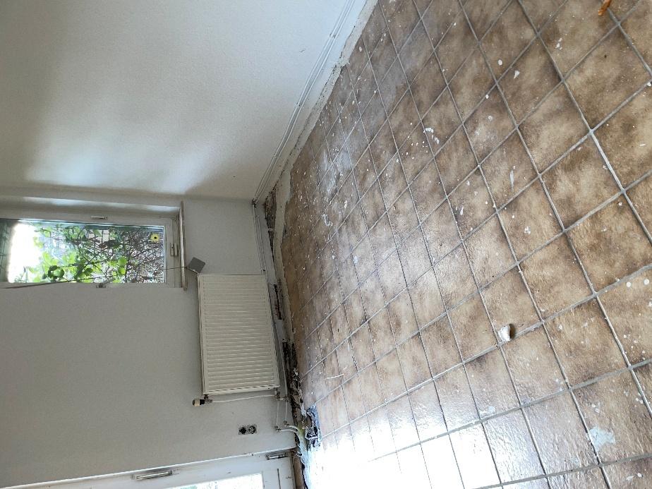 Badezimmer mit braunen Fliesen, Heizkörper und Fenster, leicht verschmutzt und in Renovierungsbedarf
