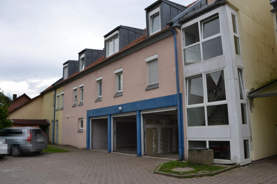 Seitenansicht eines Mehrfamilienhauses mit Garagenstellplätzen, Fenstern und Dachgauben an der Maulacher Straße