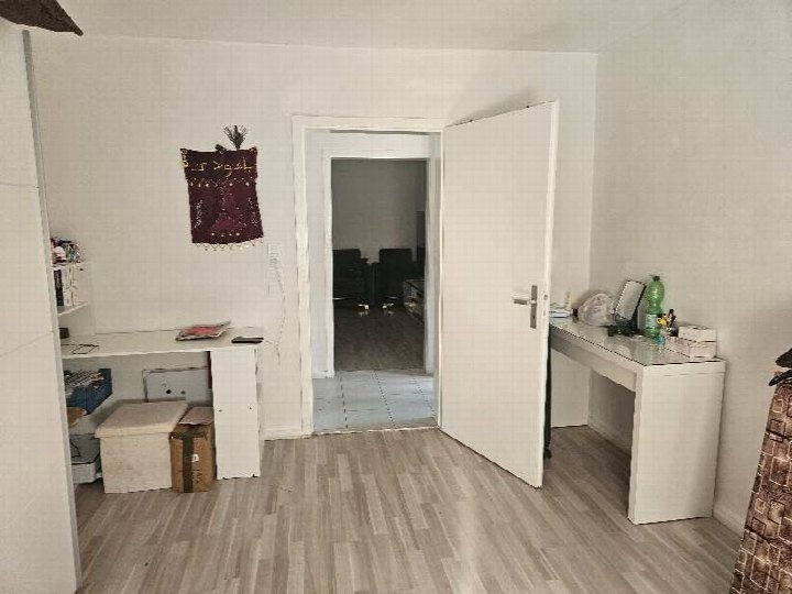 Innenraum eines Einfamilienhauses in Augsburg, Flurstraße 25, mit Holzdielenboden, weißer Tür, Schreibtisch und Regal. Im Hintergrund weitere Räume sichtbar