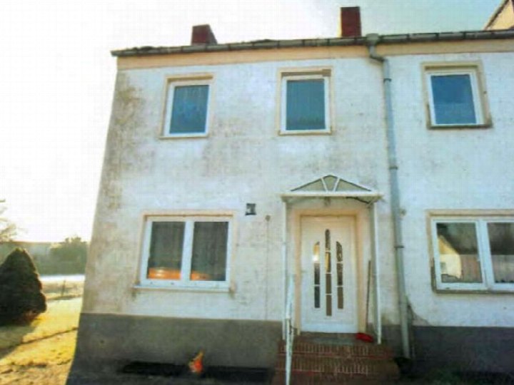 Zweistöckiges Reihenhaus in Zemitz, Neubaugebiet 11, mit weißer Fassade, mehreren Fenstern und Eingangstür mit Vordach. Grundstück mit freiem Gelände im Vordergrund