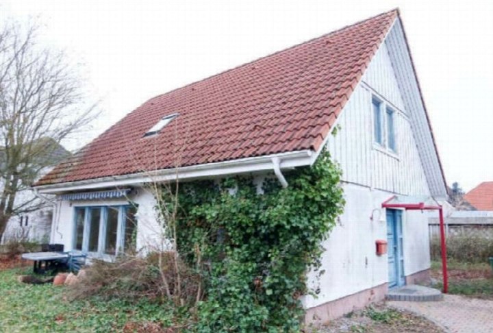 Einfamilienhaus in Trassenheide, Birkenweg 6, mit rotem Ziegeldach, weißer Fassade und Efeubewuchs an der Seite. Vordere Ansicht mit blauer Tür und Fenstern