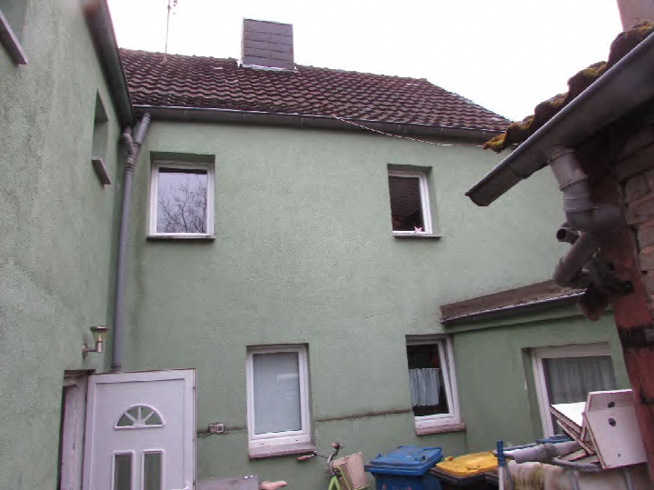 Rückansicht eines Einfamilienhauses mit grüner Fassade, Ziegeldach, Fenstern und einer Tür im Hofbereich