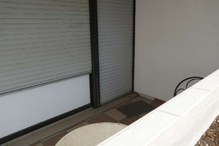 Balkon mit Fliesenboden, geschlossenem Rollladen und Teilansicht einer Brüstung