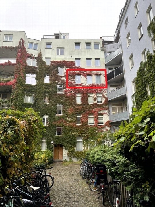 Rückansicht eines Mehrfamilienhauses mit Efeubewuchs, Innenhof mit Fahrrädern, Wohnung im roten Kasten hervorgehoben