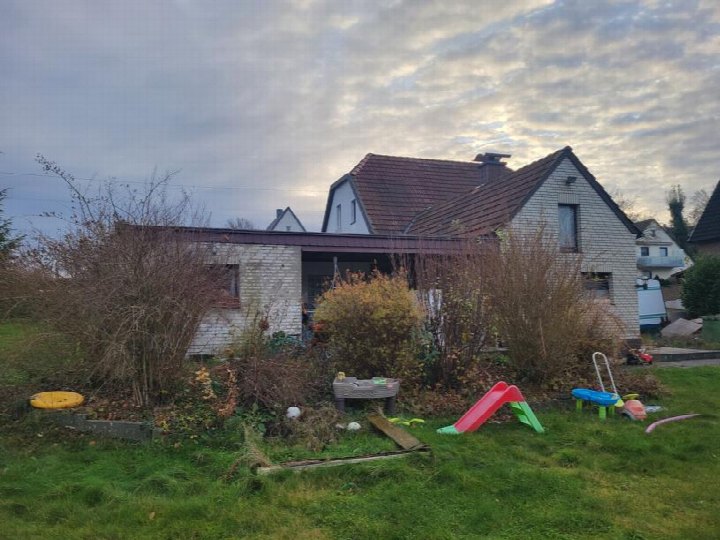 Gartenbereich eines Einfamilienhauses mit Grünfläche, Sträuchern und Kinderspielgeräten