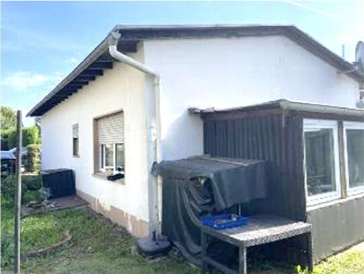 Seitenansicht eines Einfamilienhauses mit weißer Fassade, Fenstern, Dachrinne und angrenzendem Gartenbereich