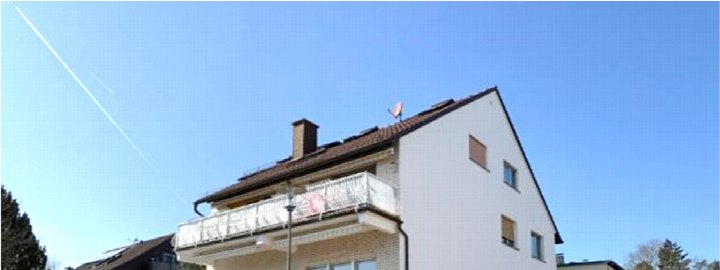 Seitenansicht eines zweistöckigen Wohnhauses mit Balkon, Dach und Schornstein unter klarem Himmel