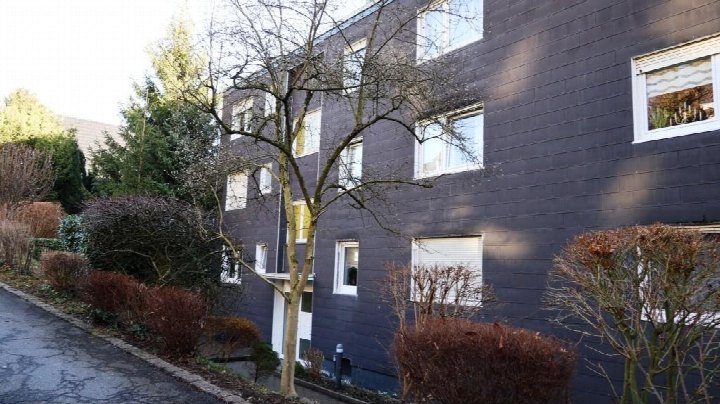 Seitenansicht eines Mehrfamilienhauses mit dunkler Fassade, Fenstern und Beeten mit Sträuchern in Gevelsberg, Südstraße