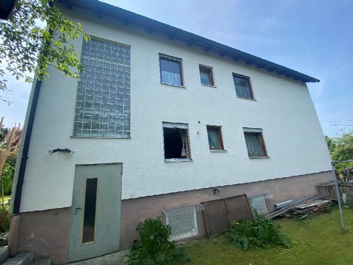 Seitenansicht eines zweistöckigen Wohnhauses mit Fenstern, einer Tür und Gartenfläche im Vordergrund