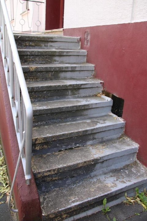 Außenstiege aus Beton mit Metallgeländer an einer roten Wand, führt zu einem Eingangsbereich