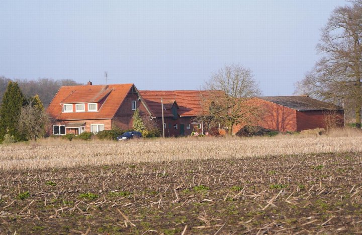 Seitenansicht eines roten Backsteinhauses mit Satteldach, umgeben von abgeerntetem Ackerland in Bruchhausen-Vilsen